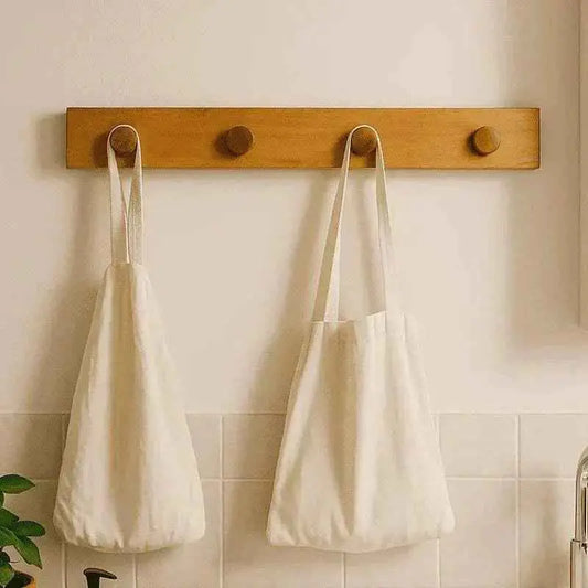 Teak hook rack with wooden pegs holding two white cotton bags above a tiled splashback