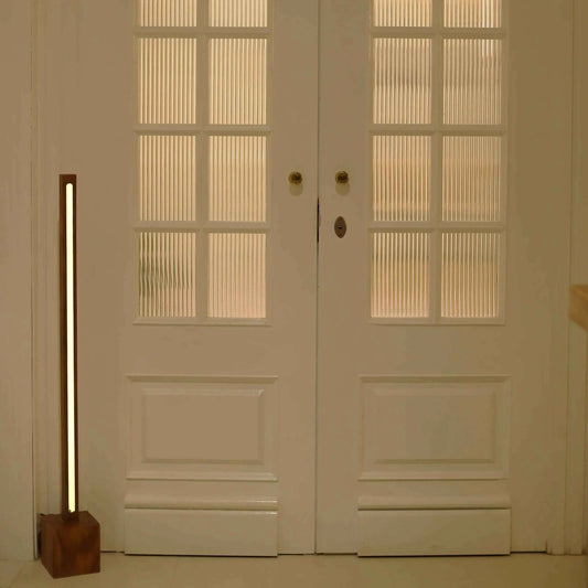Wooden floor lamp with a square block base lit beside white glass-panelled double doors