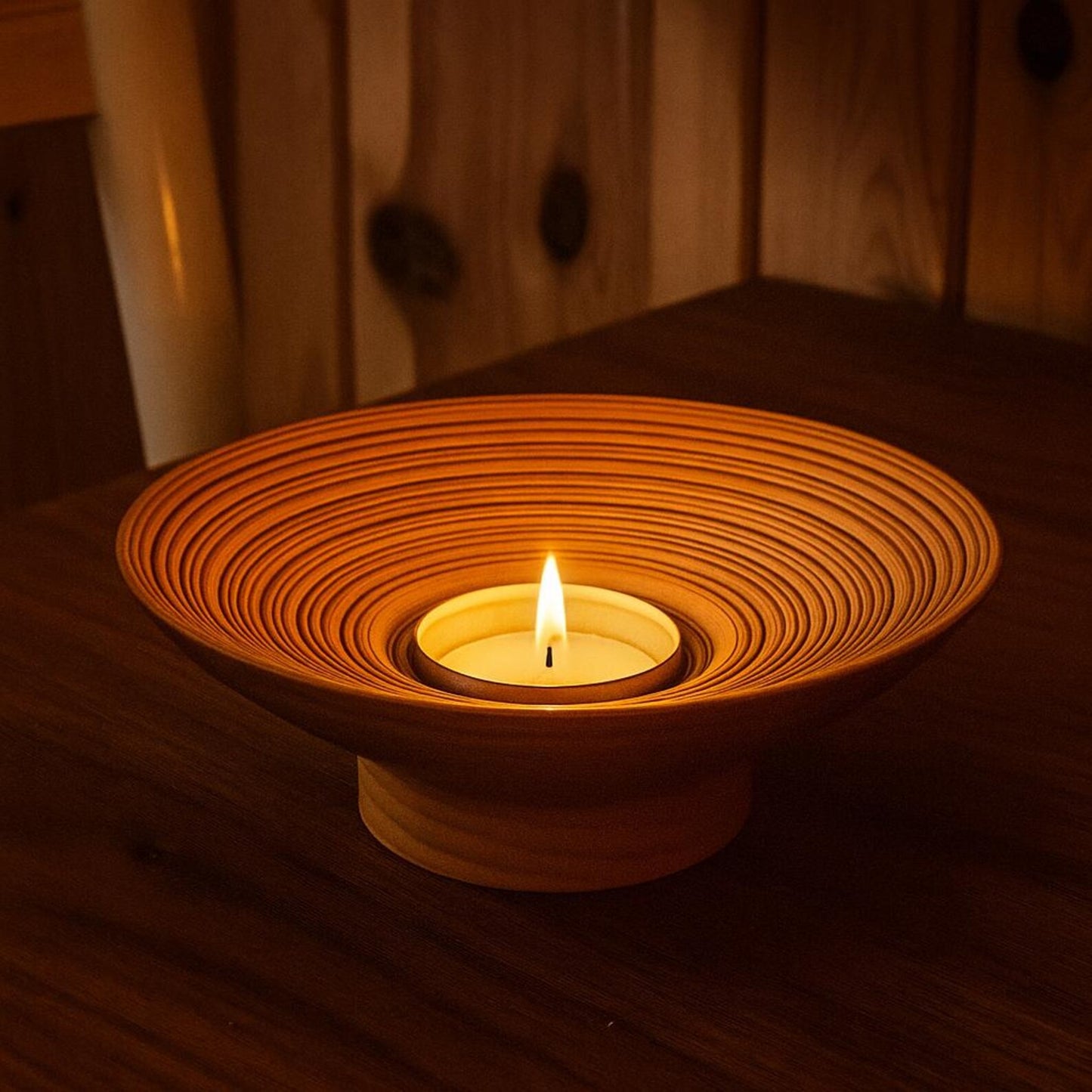 Ceramic candle holder with a lit candle on a wooden surface