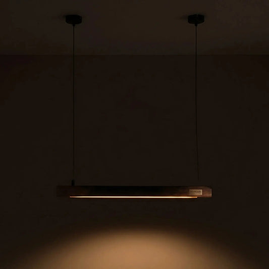 Rosewood linear pendant lit in a dark room, twin black cables from two ceiling canopies