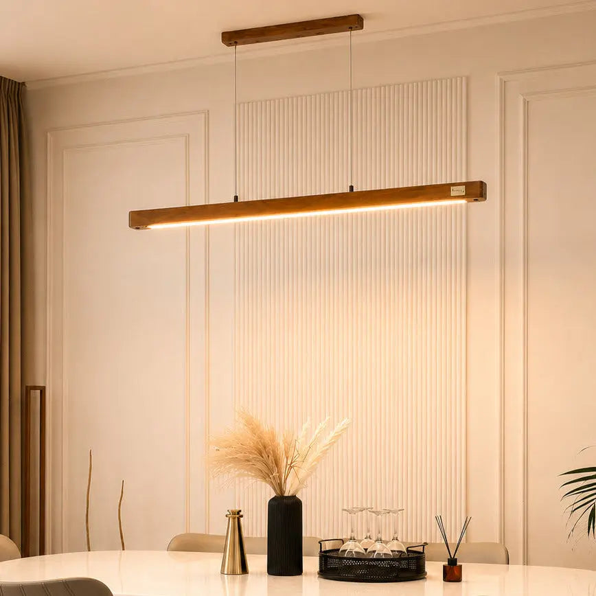 Angled view of the teak linear pendant glowing above a vase of dried pampas grass
