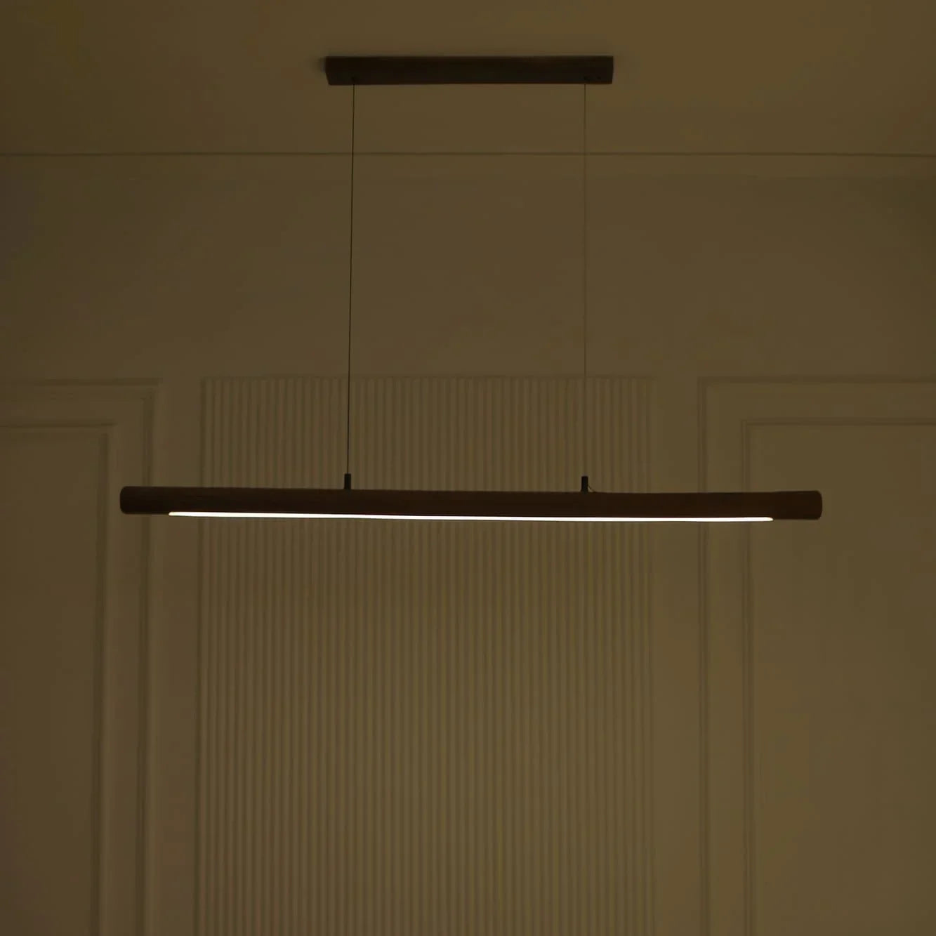 Rosewood linear pendant light casting warm light in a dim panelled room - NixWoods hanging light
