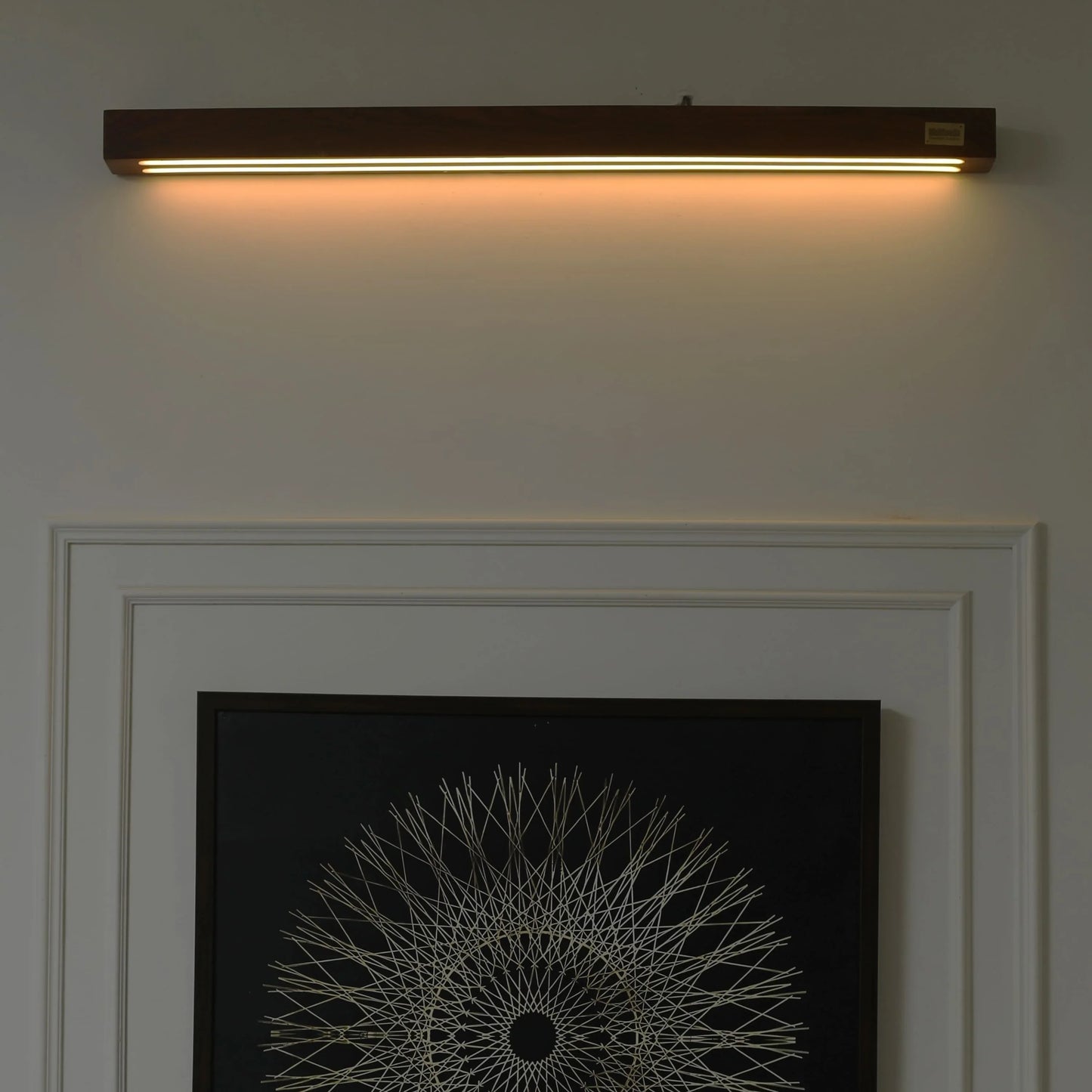 Rosewood linear wall light lit above a mantel and framed mandala art - NixWoods wooden wall sconce