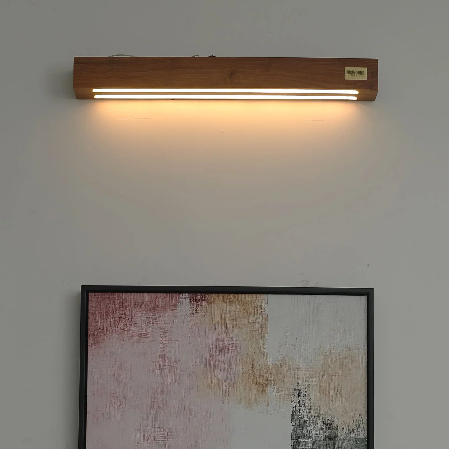 Rosewood linear wall lamp lit above framed art on a living room wall - NixWoods solid wood wall sconce
