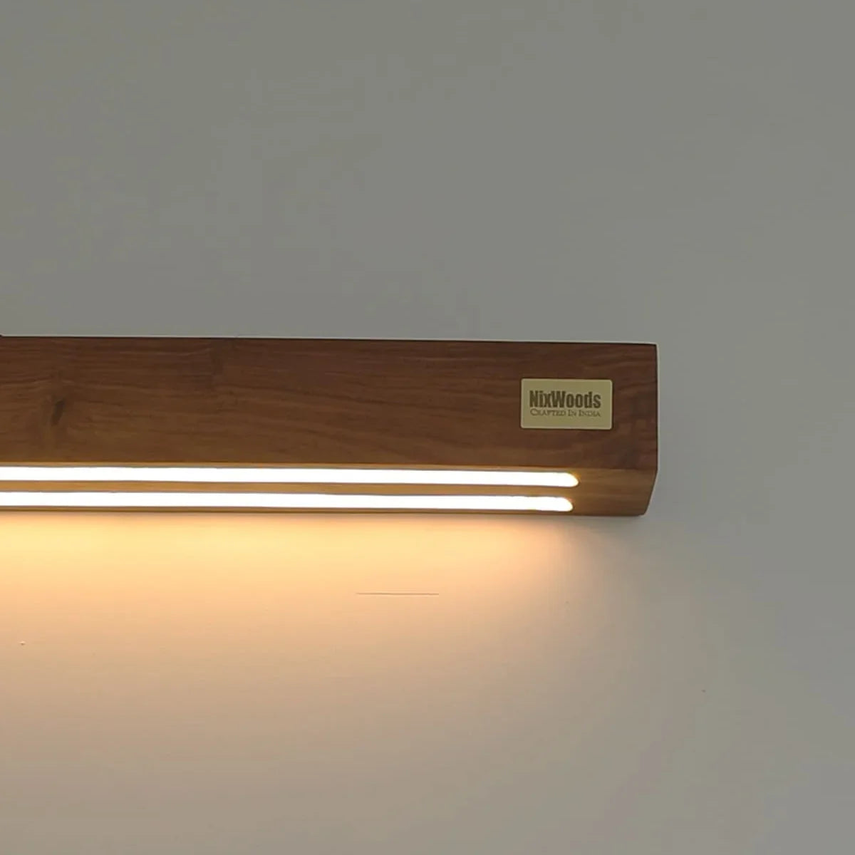 Rosewood wall sconce lit end-on, warm glow running along the solid wood body - NixWoods wall light