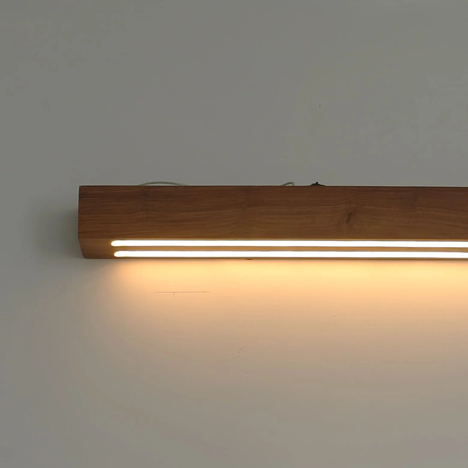Rosewood linear wall lamp lit on a plain wall with a warm downward glow - NixWoods wooden wall sconce