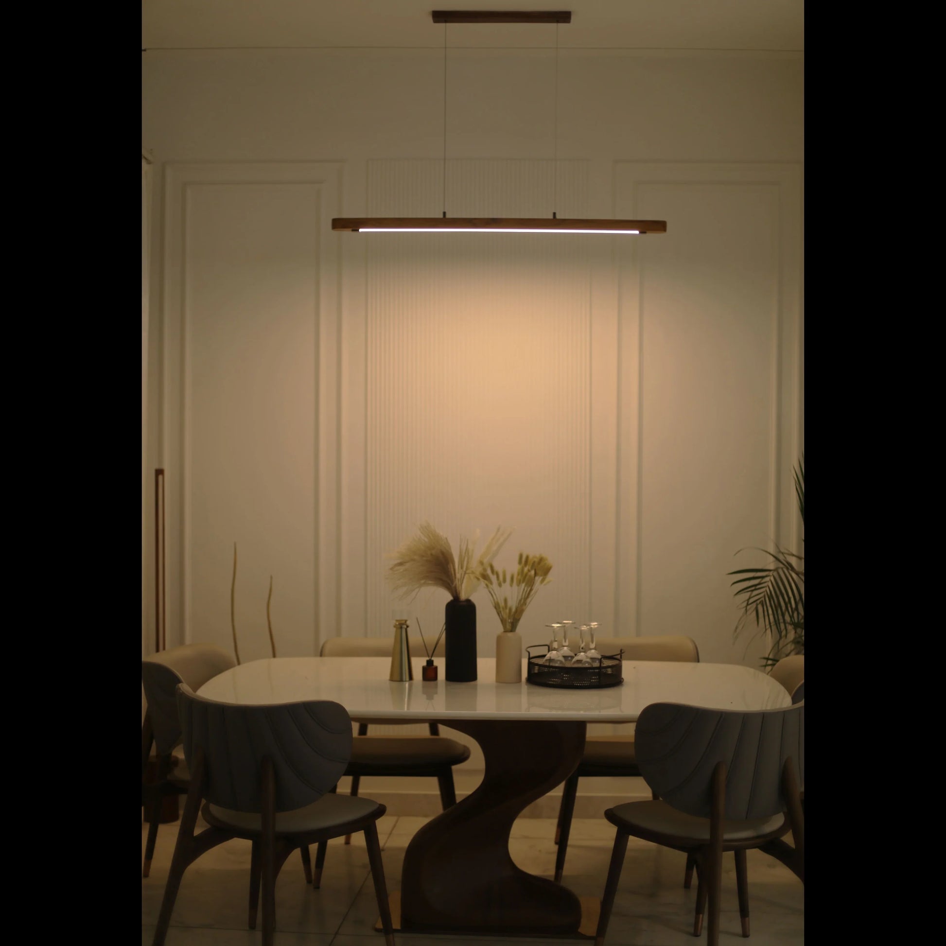 Teak linear pendant light lit above a dining table in a dark room - NixWoods hanging light