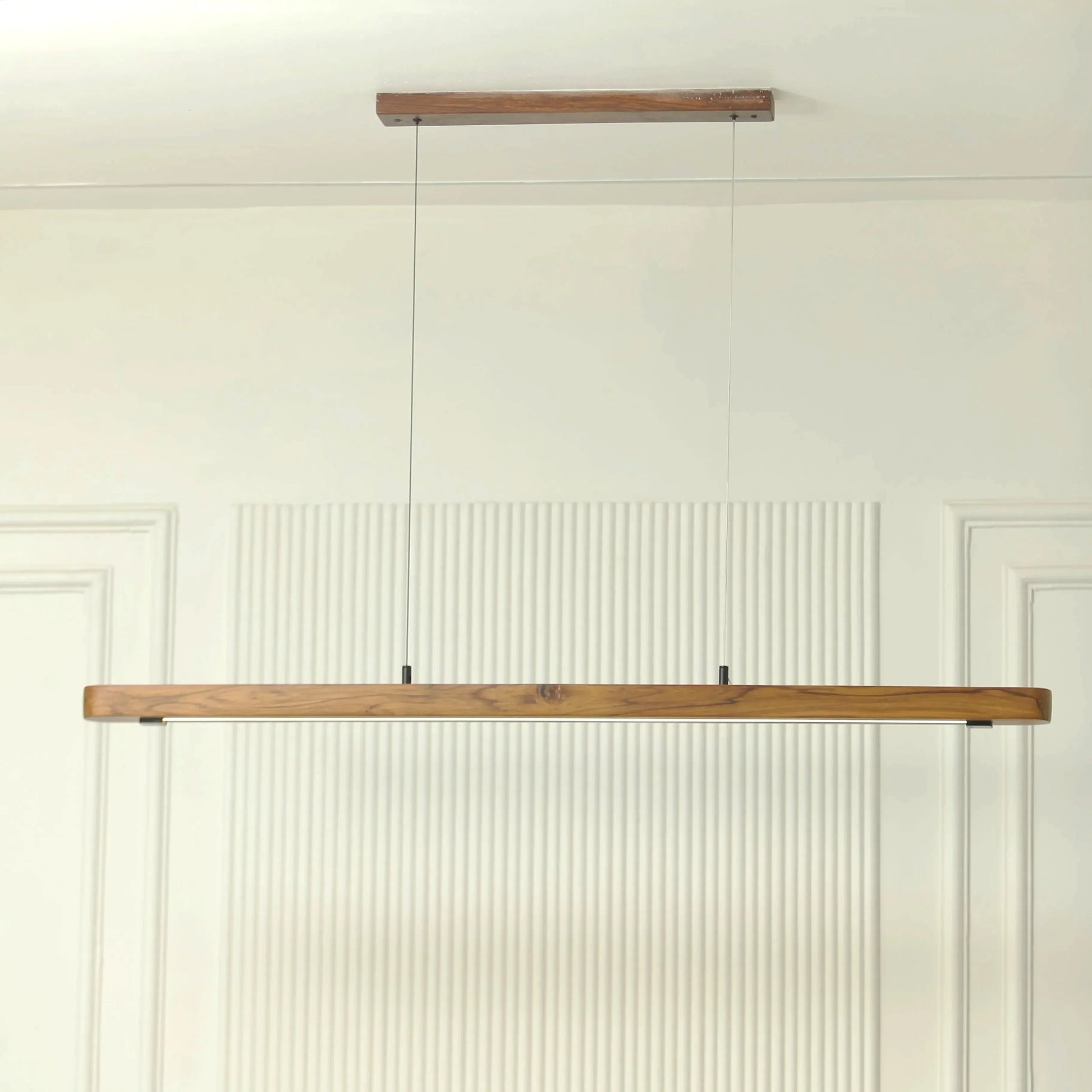 Teak wood pendant bar shown against a fluted white wall - NixWoods linear hanging light