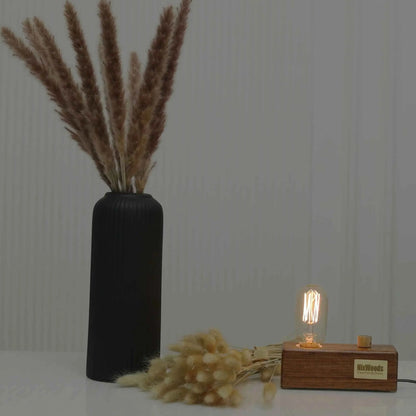 Rosewood Edison bulb lamp on a white table beside a black ribbed vase and bunny tails