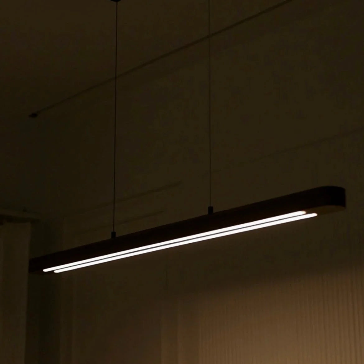 Wooden linear pendant light glowing in a darkened dining room - NixWoods handcrafted hanging light