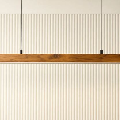 Teak linear pendant bar suspended on slim black cables in front of a fluted cream wall
