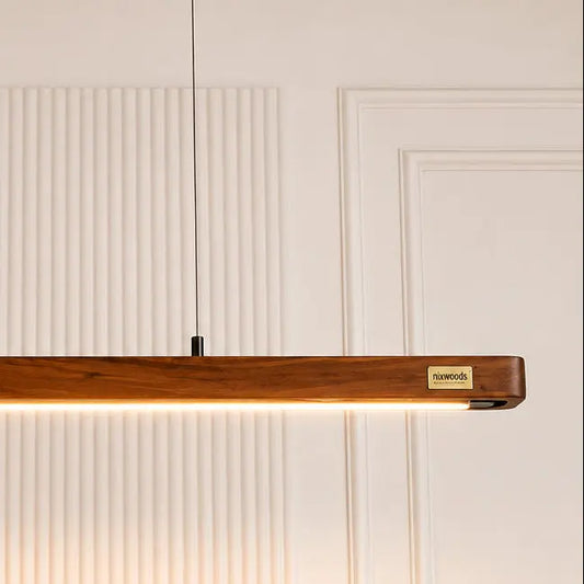 Rosewood pendant bar close-up with brass NixWoods badge and single black cable against fluted panelling