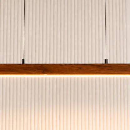 Close-up of the warm white LED strip under the teak pendant bar against a fluted wall
