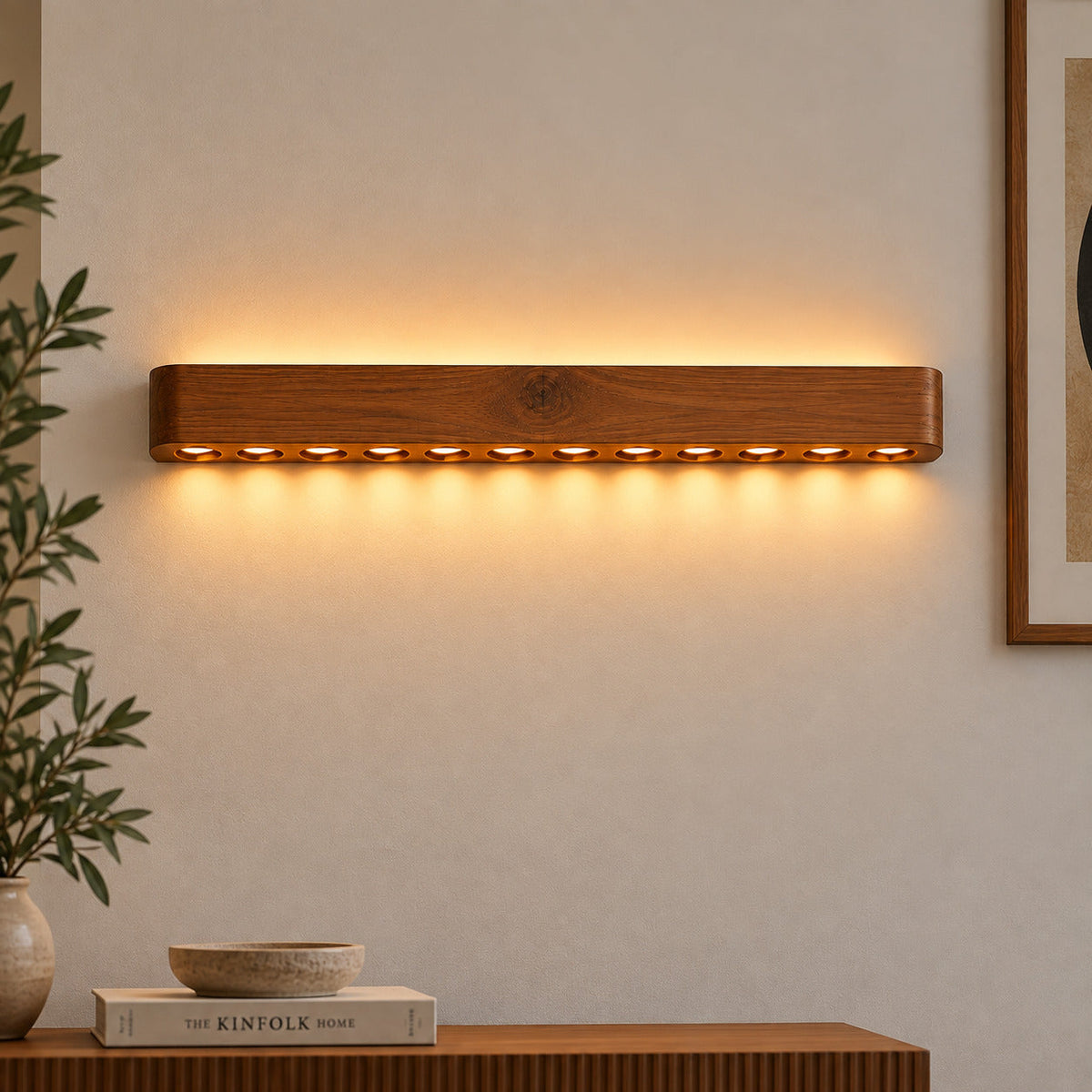Circular-hole wood wall light above a console with a bowl and books, warm dotted glow on plaster