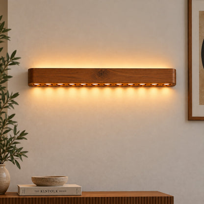 Circular-hole wood wall light above a console with a bowl and books, warm dotted glow on plaster