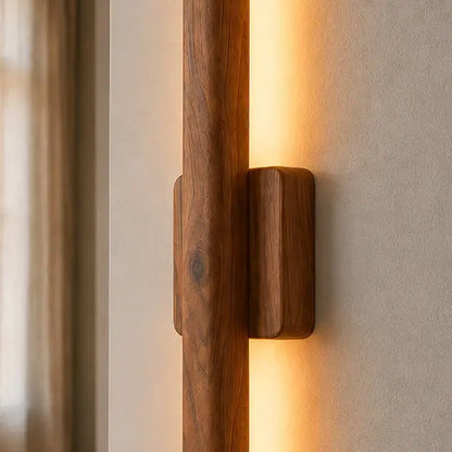 Close-up of the vertical wooden wall sconce and its mounting block, warm light on both sides