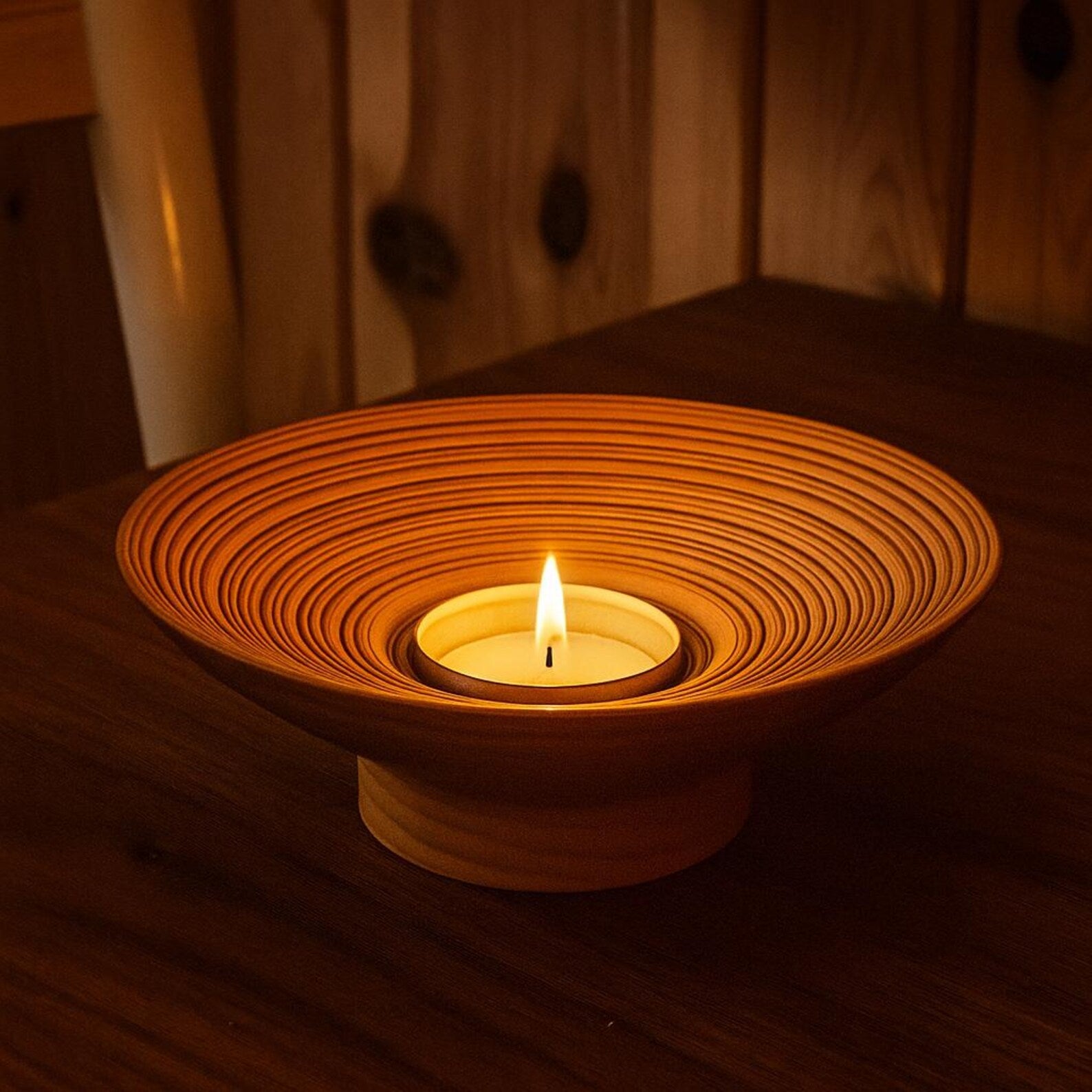 Ceramic candle holder with a lit candle on a wooden surface