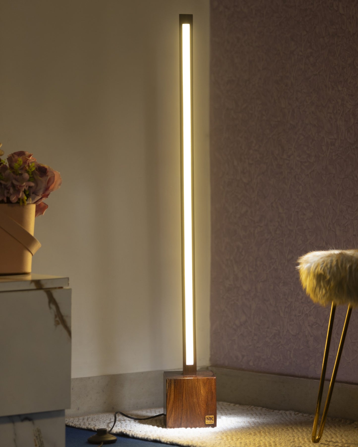 NixWoods Minimal Solid Wood Floor Lamp lit in a living-room corner - slim square rosewood rod on a solid rosewood cube base, warm ambient glow