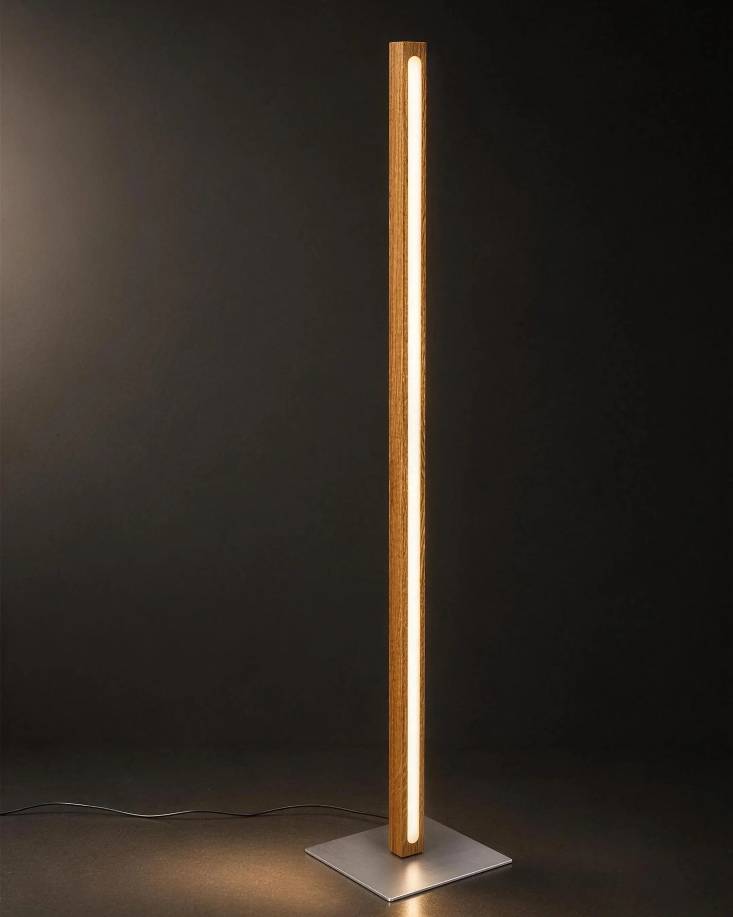 Scandinavian Teak Linear Floor Lamp lit against a dark background — the full solid teak column, warm LED line and square brushed silver base