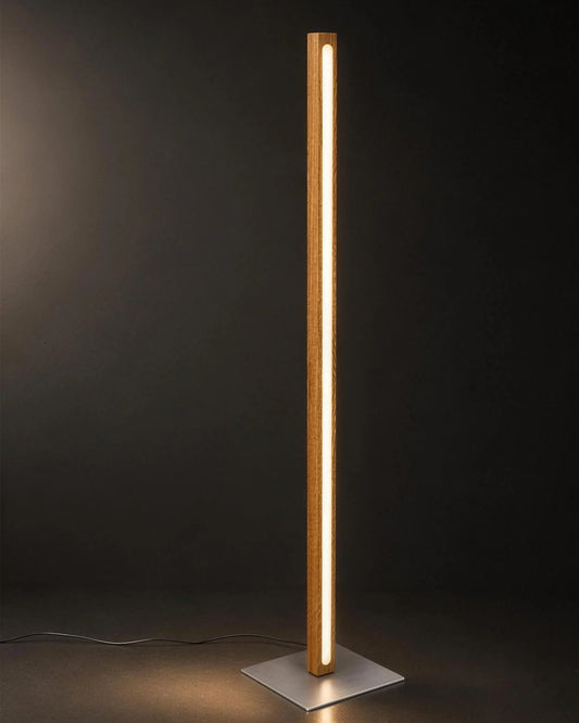 Scandinavian Teak Linear Floor Lamp lit against a dark background — the full solid teak column, warm LED line and square brushed silver base