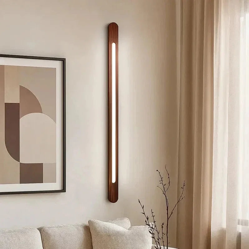 Vertical wooden wall light lit in a living room beside framed art and a sofa - NixWoods wall sconce
